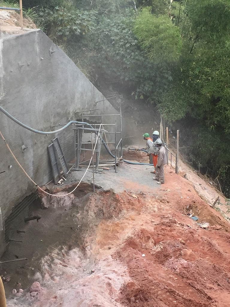 Aplicação de concreto projetado sobre talude, com malha de reforço e mangote em operação
