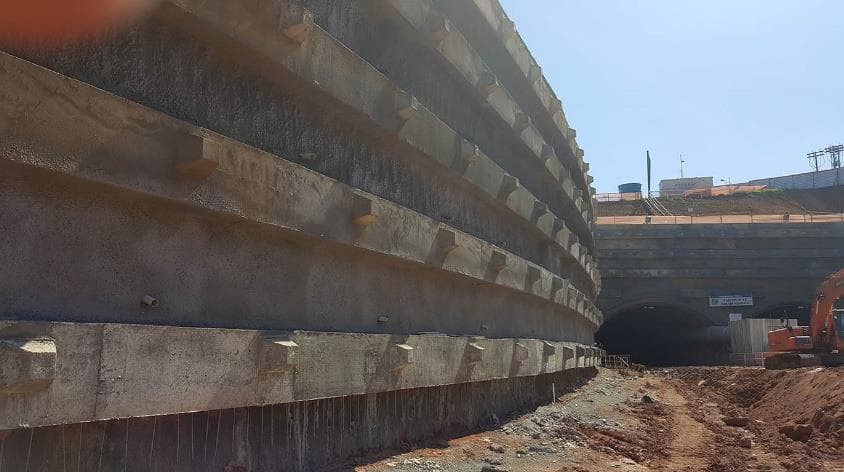 Cortina de contenção em concreto junto a portal de túnel, com faces escalonadas e barbacãs de drenagem