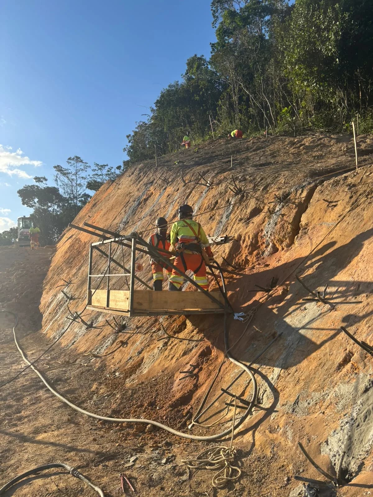 Equipe da Geobahia em plataforma suspensa executando solo grampeado, com chumbadores instalados na face do talude
